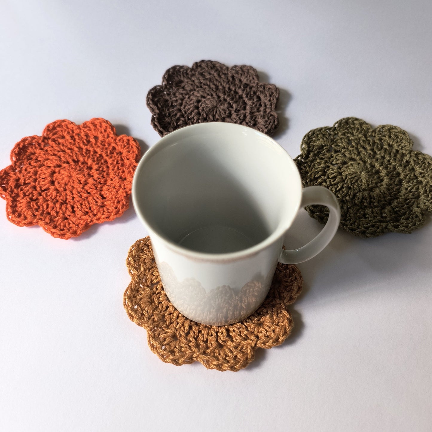 White mug on a brown crochet coaster with other coasters in the background on a white surface