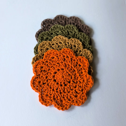 Set of four crocheted scalloped coasters in orange, brown, camel, and green on a white background.